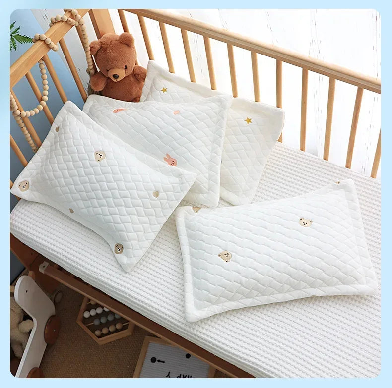 A stack of white quilted cooling pillows with small embroidered stars and hearts resting on a wooden crib railing.