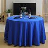 A round table set for a dinner with a blue satin cloth, wine glasses, and bottles on a dark background.