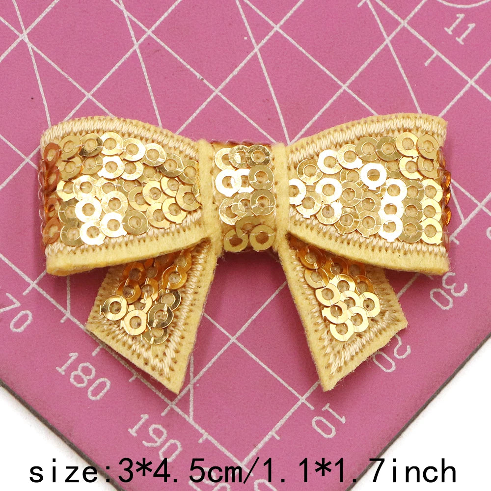 A beige sequin bow patch is shown on a pink grid background, measuring 3x4 cm or 1.1x1.7 inches.