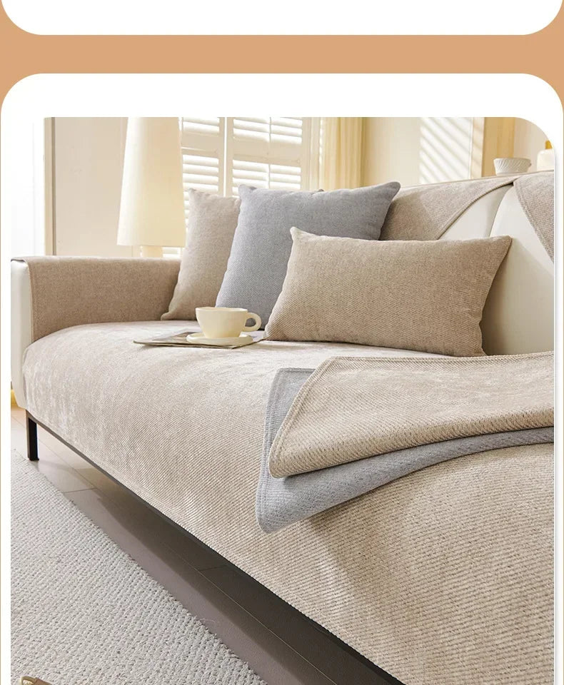 A beige waterproof anti-scratch sofa protection cover is shown on a bed with light gray pillows and natural light.