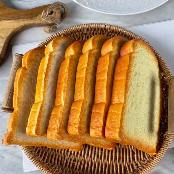 A stack of golden brown toast slices arranged on a woven basket with a wooden cutting board.