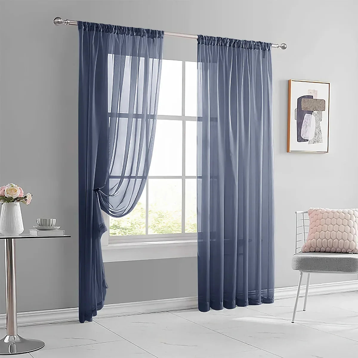 A pair of long, blue sheer curtains with rod pockets hanging in a window frame.