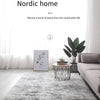 A light gray tie-dyed plush floor mat placed on a wooden floor in a bright, minimalist living space.