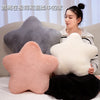 A woman is sitting on a couch surrounded by various star-shaped decorative throw pillows in pink, gray, and white.