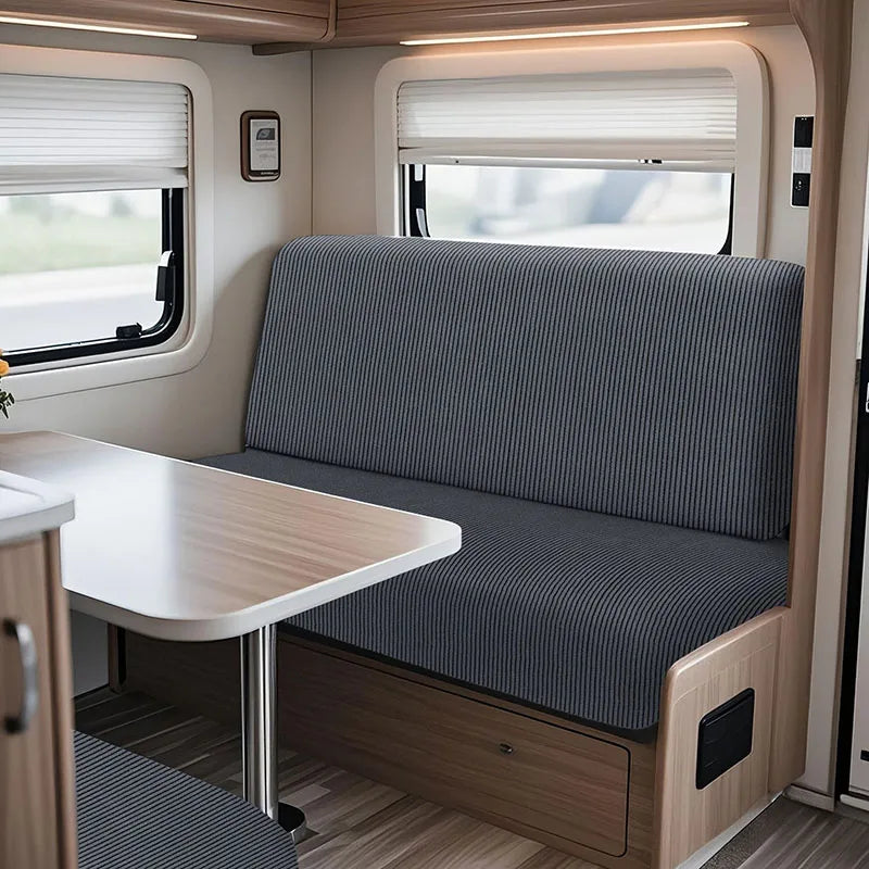 Interior view of an RV dinette with a gray upholstered bench seat and a light wood table.