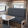 Interior view of an RV dinette with a gray upholstered bench seat and a light wood table.