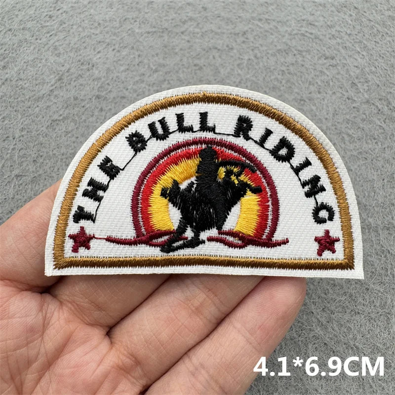 An embroidered patch featuring a bull riding theme with a silhouette of a rider in black and yellow against a red background.