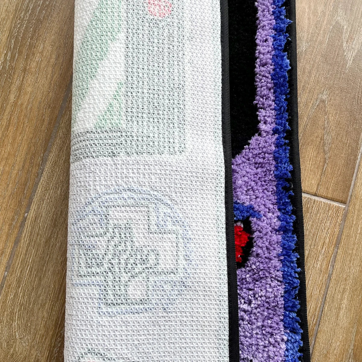 A close-up of a tufted floor mat featuring white and purple fibers with colorful accents.