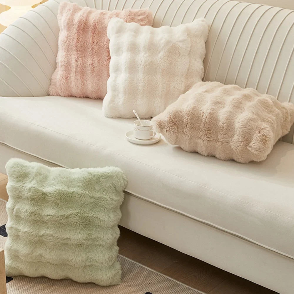 A collection of fluffy, pastel-colored cushion covers in pink, cream, and pale green resting on a white sofa.