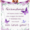 A woman in a pink top holds a white blanket featuring a floral design and the text We hope every time you snuggle this blanke