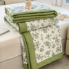 A stack of light green floral printed summer quilts folded on a white bed sheet.
