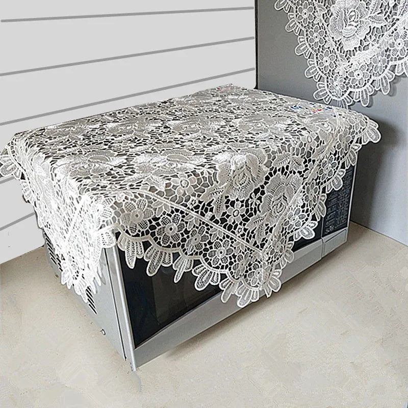 A table covered with a white floral lace tablecloth displayed on a modern glass table.