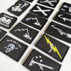 A collection of black embroidered patches featuring skull, pirate, and sword designs with hook and loop backing.