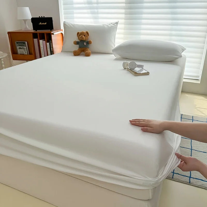 A white fitted bed sheet cover is being adjusted on a white bed, with pillows and a teddy bear visible.
