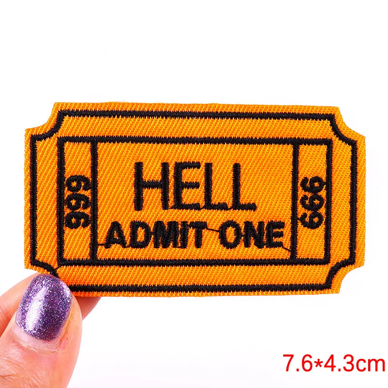 An orange embroidered letter patch with the text HELL ADMIT ONE on a black background.