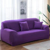 A deep purple stretch sofa cover with two matching pillows placed in a bright living room.