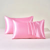 A set of two pink satin pillows resting on a white surface.
