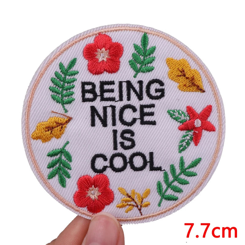 Round embroidered patch with a pink background featuring the text BEING NICE IS COOL surrounded by green and yellow leaves.