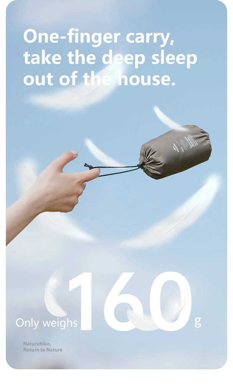 A hand holds a small, dark gray inflatable pillow against a light blue sky.