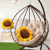 A beige sunflower shaped throw pillow rests inside a dark metal hanging chair.