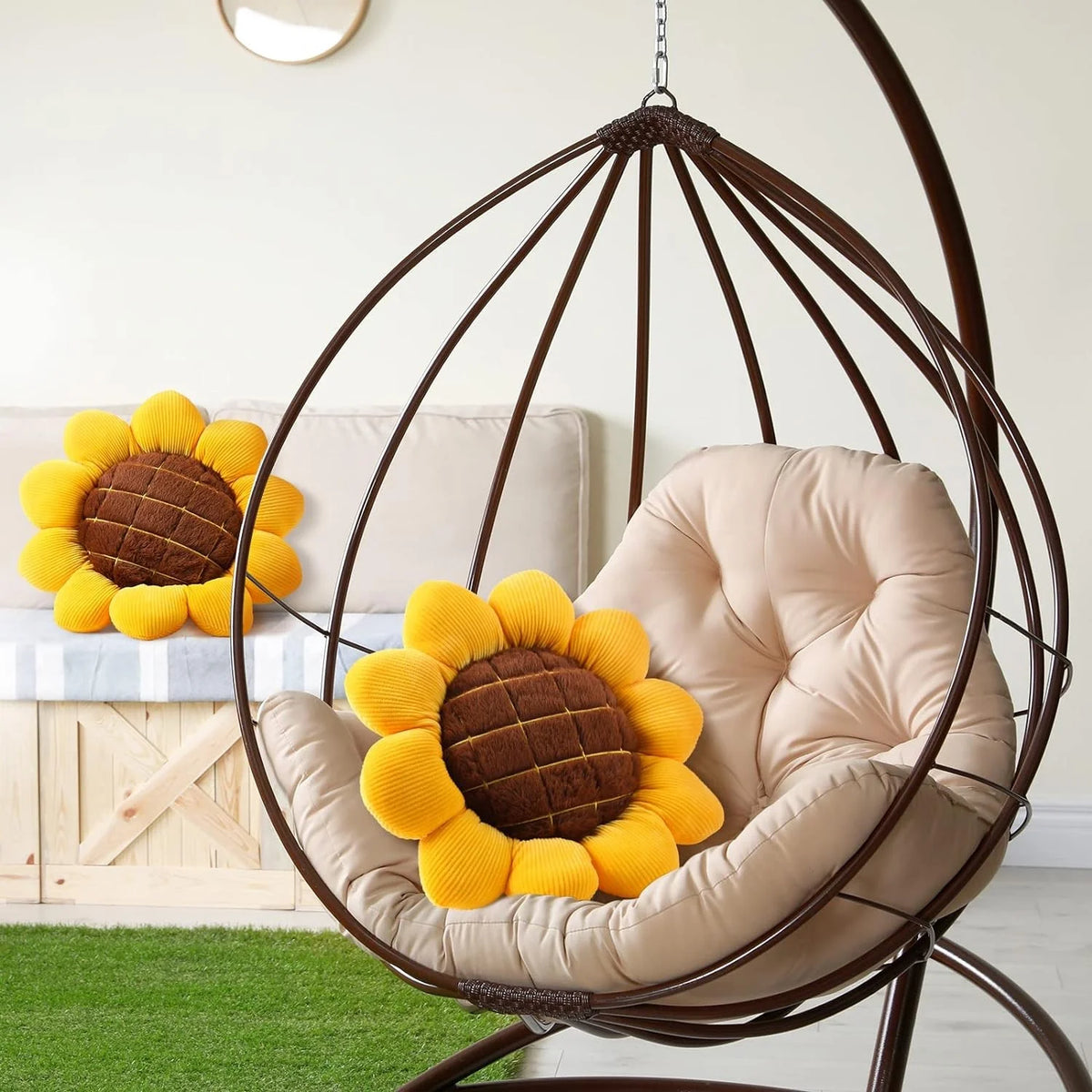 A beige sunflower shaped throw pillow rests inside a dark metal hanging chair.