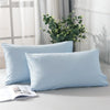 Two light blue microfiber pillow covers displayed on a white surface with greenery in the background.