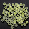 A pile of small, translucent light green glass seed beads with a glow-in-the-dark effect.