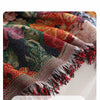 A close-up of a richly colored floral jacquard tasseled sofa throw blanket with fringed edges.