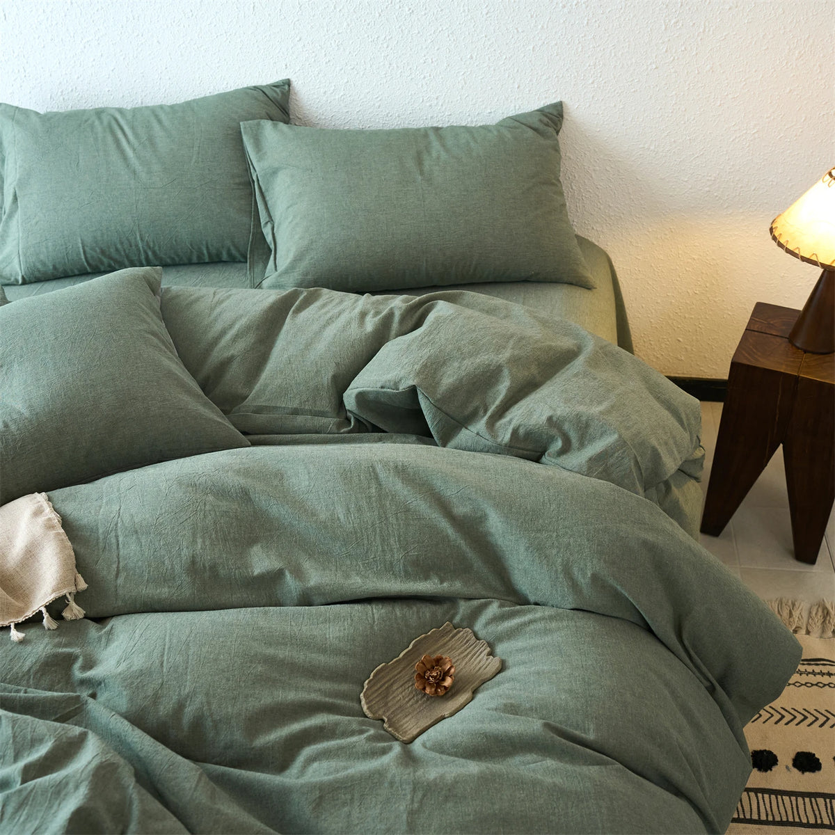 A teal cotton yarn-dyed duvet cover with matching pillows and a wooden lamp on a bed.