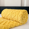 A rolled yellow ultra-soft coral fleece blanket resting on a white surface.