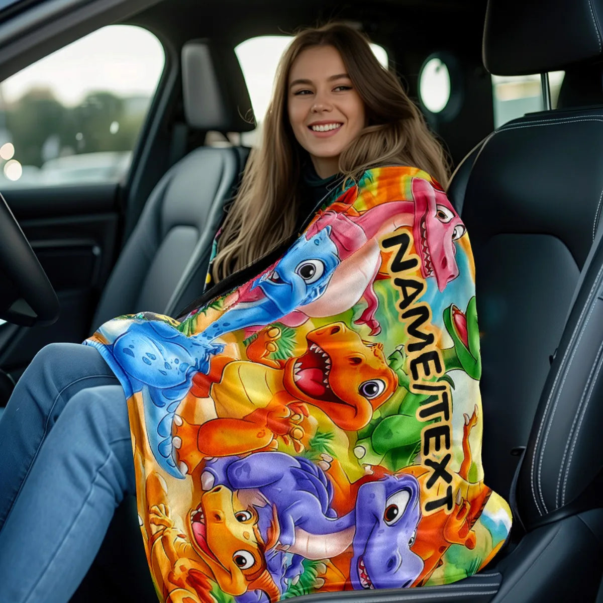 A young woman is sitting in a car, holding a colorful blanket featuring cartoon dinosaurs.