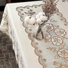 A white dining table cloth with a lace pattern is set with dried floral arrangements and fluffy white pom-poms.