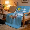 A blue plush throw blanket featuring a C-Curious George character climbing a string toward clouds.