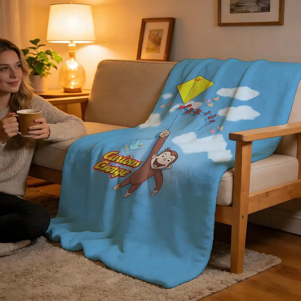 A blue plush throw blanket featuring a C-Curious George character climbing a string toward clouds.