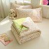 A quilted blanket in pale pink with a floral pattern is folded on a white surface next to a small stuffed animal.