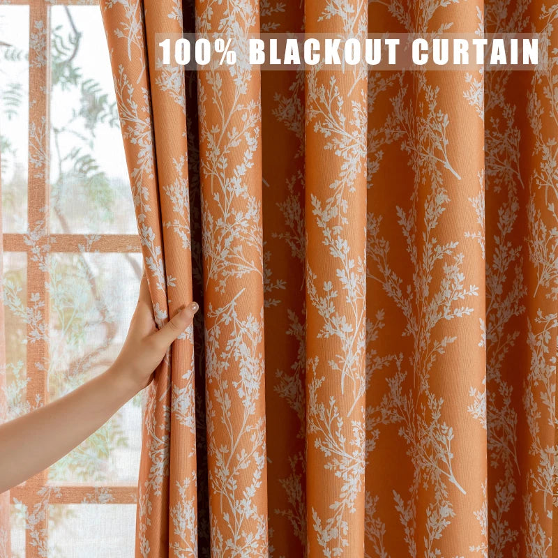 Orange blackout curtain fabric with white floral pattern hanging in a window.