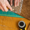 A hand uses a pencil to mark measurements on a precision acrylic quilting ruler placed on a wooden surface.