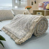 A rolled light gray linen quilt blanket with a ruffled edge resting on a light blue surface.