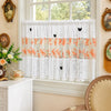 White lace cafe curtain with orange floral embroidery and black butterfly appliqués hanging in a window.