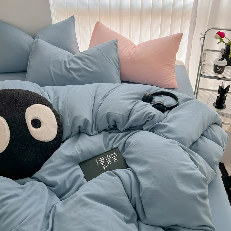 A light blue duvet cover set with matching pillows and a black stuffed animal on the bed.