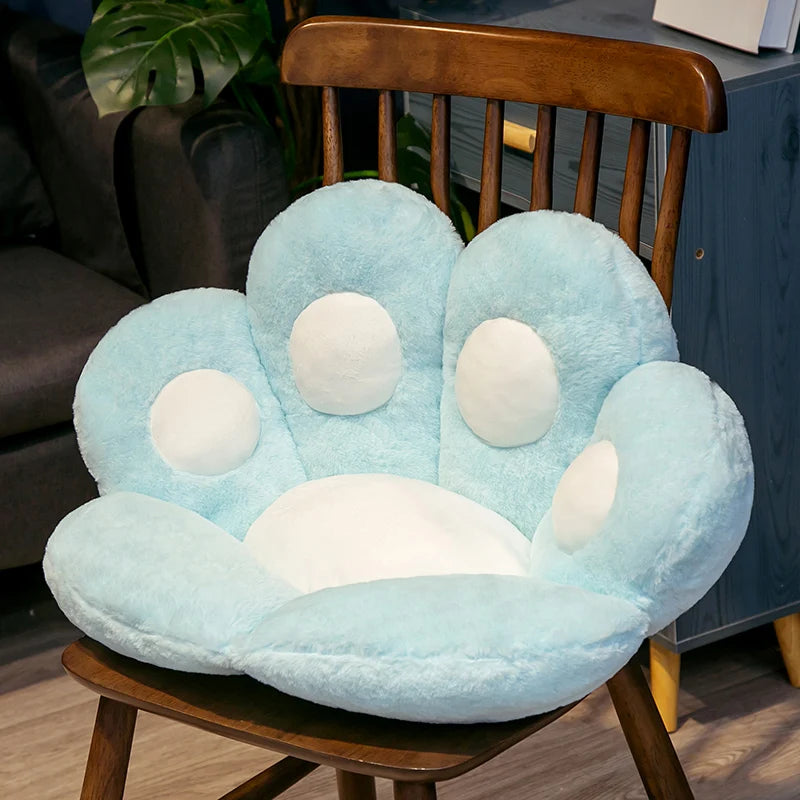 A light blue plush bear paw cushion resting on a wooden chair.