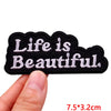 Black embroidered patch with white text that reads Life is Beautiful
