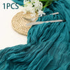 A teal fabric table runner made of semi-sheer gauze is draped next to a gold woven mat and silverware.