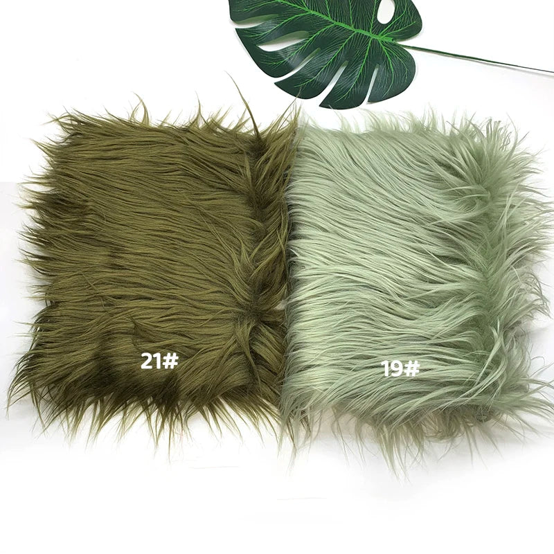 Two swatches of faux fur fabric, one olive green and one pale mint green, displayed next to a monstera leaf.
