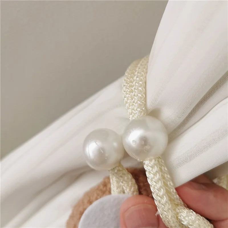 Close-up of cream colored pearl tiebacks used to secure a white curtain fabric.