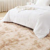 A fluffy cream tie-dye shaggy rug placed on a light wooden floor next to a white bed.