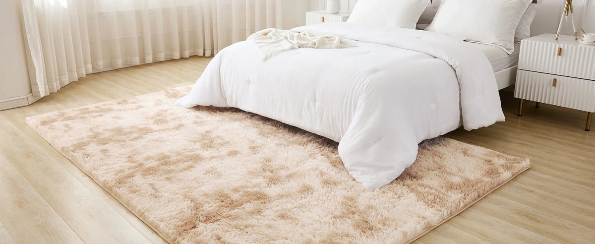 A fluffy cream tie-dye shaggy rug placed on a light wooden floor next to a white bed.