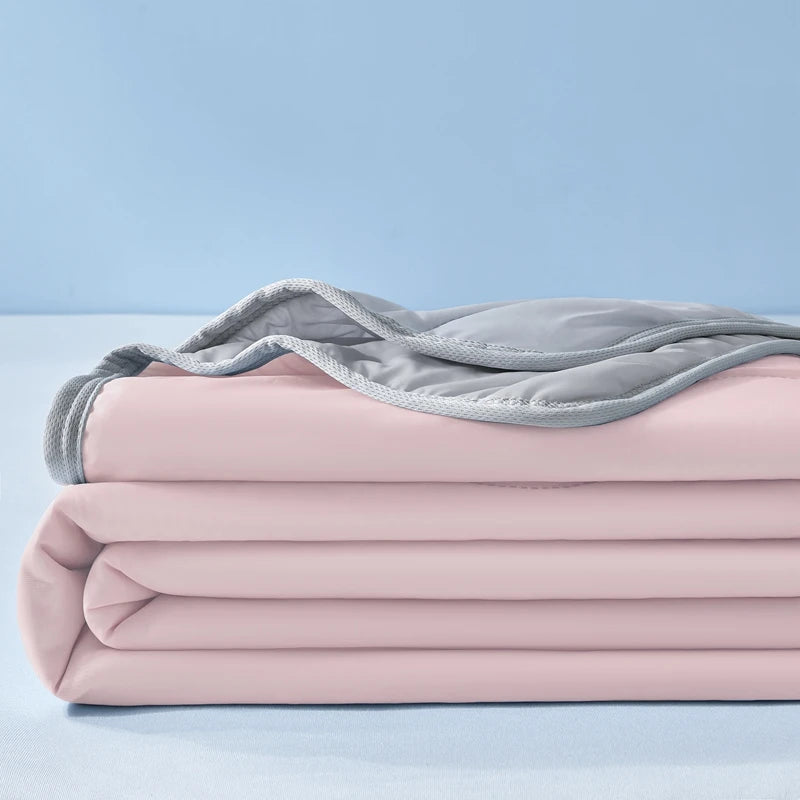 Pink cooling fiber blankets stacked and folded on a light blue surface with a gray blanket draped on top