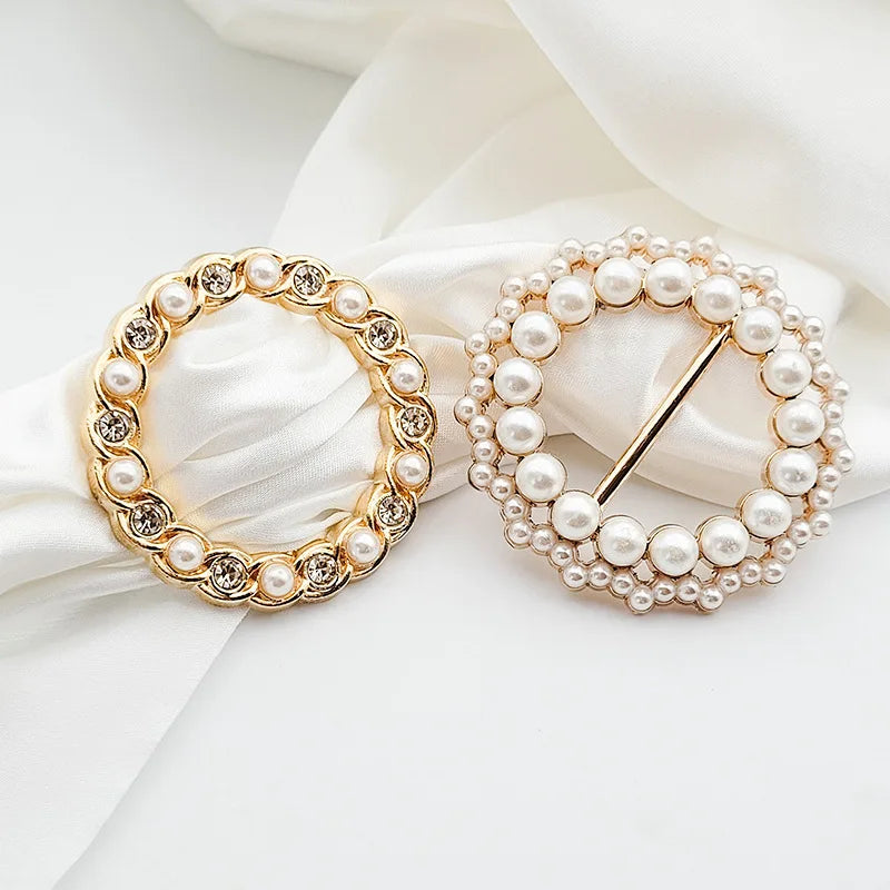 Gold-toned metal ring clips encrusted with white pearls displayed on a white fabric background.