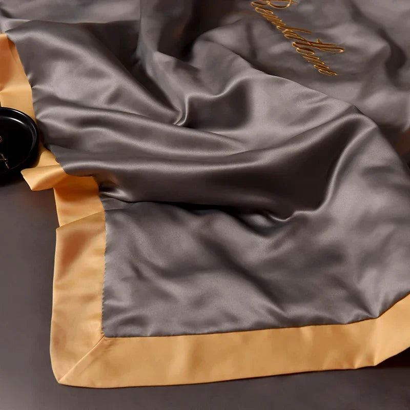 A luxurious gray ice silk blanket set with gold trim and embroidery is draped softly.